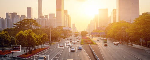 Cars highlighted by artificial intelligence driving down highway with high-rise buildings in the distance